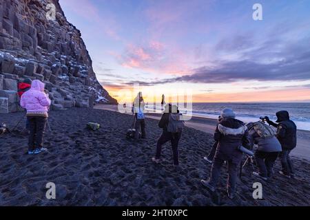Fotografen, die den dramatischen Sonnenaufgang über dem Reynisfjara Black Sand Beach in der Nähe des Dorfes Vík i Myrdal im Südosten Islands festhalten Stockfoto