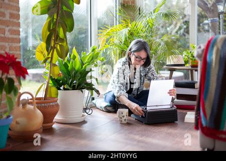 Erwachsene Schriftstellerin, die ein leeres Blatt Papier auf die Schreibmaschine legt. Sie ist zu Hause. Stockfoto