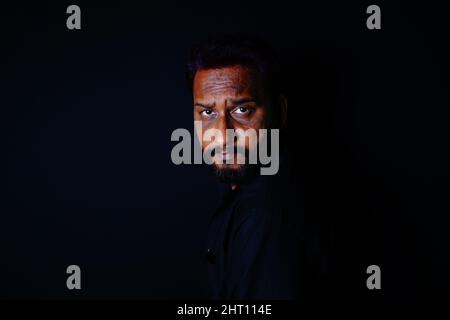 Nahaufnahme eines bärtigen Indianers in schwarzem Hemd auf schwarzem Hintergrund Stockfoto