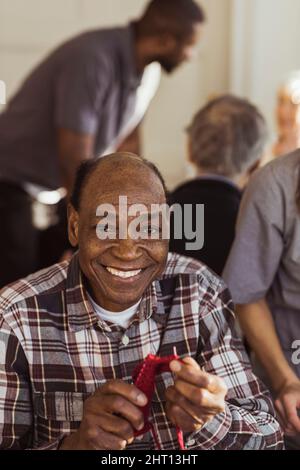 Porträt eines lächelnden älteren Mannes, der im Altersheim strickt Stockfoto