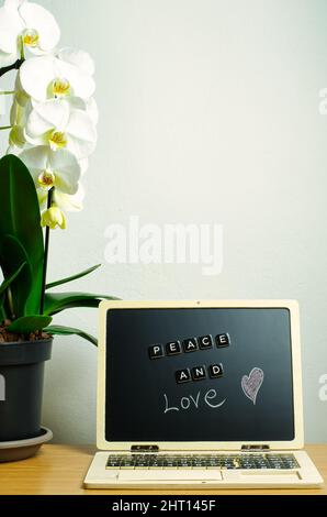 Vertikales Foto mit Botschaft von Frieden und Liebe. In der Komposition befinden sich eine weiße Orchidee und eine Arbeitsstation mit Schreibtisch. Stockfoto