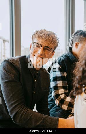 Porträt eines lächelnden blonden Mannes mit Brille, der in der Cafeteria der Universität sitzt Stockfoto