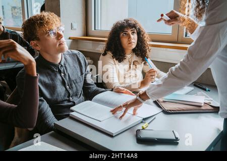 Mittelteil des Lehrers, der jungen Studenten im Klassenzimmer der Universität hilft Stockfoto