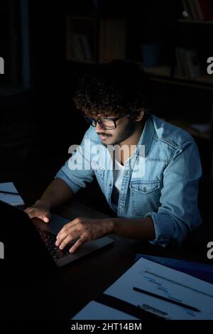 Junger indischer Geschäftsmann, Student, der nachts mit einem Laptop online arbeitet. Stockfoto