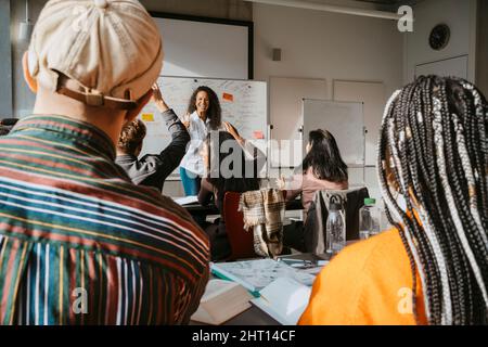 Glücklicher Professor, der Studenten mit erhobenen Händen im Klassenzimmer ansieht Stockfoto