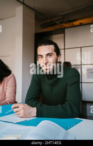 Porträt eines jungen männlichen Studenten, der mit einer Akte an der Community College sitzt Stockfoto