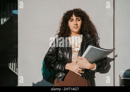 Porträt einer jungen Frau, die ein Buch an einer grauen Wand hält Stockfoto