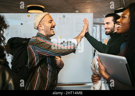 Fröhliche männliche Freunde geben High-Five von Frau lachend in der Hochschule Stockfoto