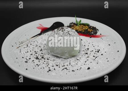 Ein traditionelles japanisches Dessert Mochi mit Schokoladensorbet, Gelatine aus Reis in einem verzierten Teller mit Zuckerpulver auf schwarzem Hintergrund. Stockfoto