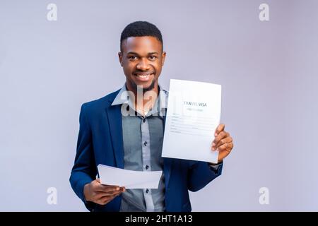Ein afrikanischer Geschäftsmann lächelt, während er seine Papiere isoliert auf weißem Hintergrund hält Stockfoto