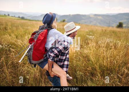 Ein junges, glückliches Paar in der Liebe hat Spaß, während er an einem schönen sonnigen Tag auf einer Wiese spazieren geht. Wandern, Natur, Beziehung, zusammen Stockfoto