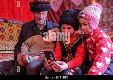 Kashgar, China. 24.. Februar 2022. (220226) -- KASHGAR, 26. Februar 2022 (Xinhua) -- Kinder sehen sich Videos mit einem Familienmitglied im Dorf Rasekam im Taxkorgan Tajik Autonomen Kreis, nordwestlich der Autonomen Region Xinjiang Uygur, am 24. Februar 2022 auf einem Mobiltelefon an. Rasekam ist ein kleiner Weiler, der sich auf dem Pamir Plateau befindet, mit einer durchschnittlichen Höhe von 3.000 Metern über dem Meeresspiegel. Früher bestand Rasekam aus 12 Gruppen von Hirten, die verstreut in der Bergregion residierten, war das Dorf arm an Transport und Lebensunterhalt. Seit 2017 hat die lokale Regierung damit begonnen, Einheimische zu verlagern Stockfoto