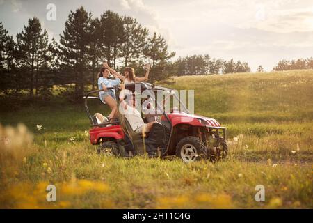 Freunde jubeln und genießen einen schönen sonnigen Tag, während sie mit einem Geländewagen in die Natur der Berge fahren. Freiheit, Freundschaft, Glück, Naturkonz Stockfoto