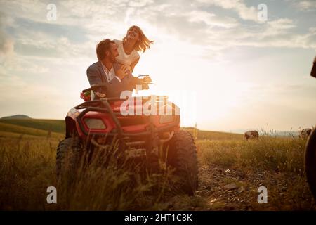 Junge frisch verheiratetes Paar, die eine gute Zeit haben, während sie eine Quad-Fahrt bei einem wunderschönen Sonnenuntergang in der Natur genießen. Reiten, Hochzeit, Natur, Aktivität Stockfoto