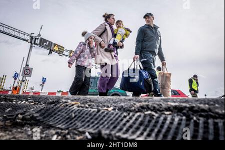 Przemysl, Polen. 26.. Februar 2022. Eine Grenzwache trägt ein Flüchtling aus der Ukraine ihr Gepäck, nachdem sie die Grenze von Shehyni in der Ukraine nach Medyka in Polen überschritten hat. Viele Ukrainer verlassen das Land nach militärischen Aktionen Russlands auf ukrainischem Territorium. Quelle: Michael Kappeler/dpa/Alamy Live News Stockfoto