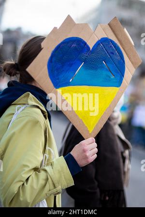 Stuttgart, Deutschland. 26.. Februar 2022. Während einer Demonstration gegen den russischen Militäreinsatz in der Ukraine hält eine Frau am Wilhelmsplatz ein Zeichen mit einem Herz in den Farben der Ukraine in der Hand. (Recrop) Quelle: Christoph Schmidt/dpa/Alamy Live News Stockfoto