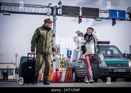 Przemysl, Polen. 26.. Februar 2022. Eine Grenzwache hilft einem Flüchtling aus der Ukraine mit ihrem Gepäck, nachdem sie die Grenze von Shehyni in der Ukraine nach Medyka in Polen überquert hat. Viele Ukrainer verlassen das Land nach militärischen Aktionen Russlands auf ukrainischem Territorium. Quelle: Michael Kappeler/dpa/Alamy Live News Stockfoto