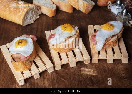 Scheibe Brot mit Speck und gegrilltem Wachtelei auf einem Holztisch. Stockfoto