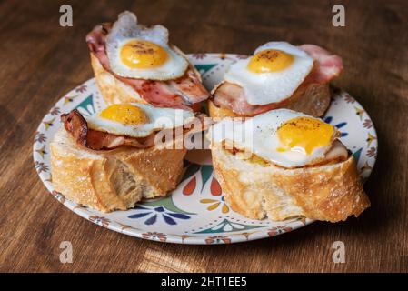 Scheibe Brot mit Speck und gegrilltem Wachtelei auf einem Holztisch. Stockfoto