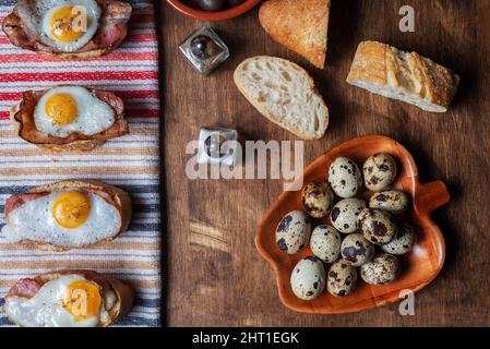 Scheibe Brot mit Speck und gegrilltem Wachtelei auf einem Holztisch. Stockfoto