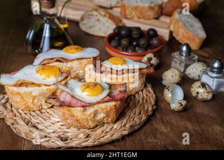 Scheibe Brot mit Speck und gegrilltem Wachtelei auf einem Holztisch. Stockfoto