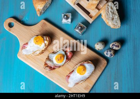 Scheibe Brot mit Speck und gegrilltem Wachtelei auf einem Holztisch. Stockfoto