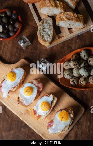 Scheibe Brot mit Speck und gegrilltem Wachtelei auf einem Holztisch. Stockfoto