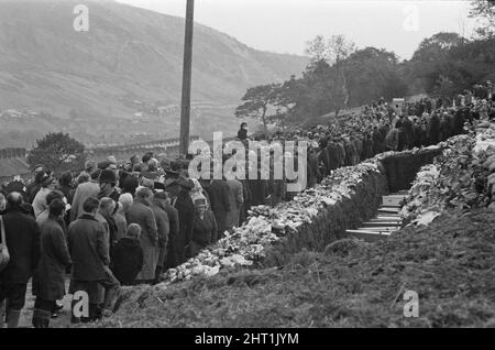 Aberfan - 27.. Oktober 1966 der Aberfan-Friedhof am Hang, eine Reihe von Särgen während der Massenbestattung. Familienmitglieder und lokale Dorfbewohner zahlen ihren Respekt. Die Katastrophe von Aberfan war ein katastrophaler Einsturz einer kollidierenden Beute im walisischen Dorf Aberfan, in der Nähe von Merthyr Tydfil. Er wurde durch eine Ansammlung von Wasser im angesammelten Fels und Schiefer verursacht, die plötzlich in Form von Schlamm bergab zu rutschen begann und am 21.. Oktober 1966 die Pantglas Junior School darunter verschlang und 116 Kinder und 28 Erwachsene tötete. Das ursprüngliche Schulgelände ist heute ein Gedenkgarten. Aufnehmen von Bildern Stockfoto