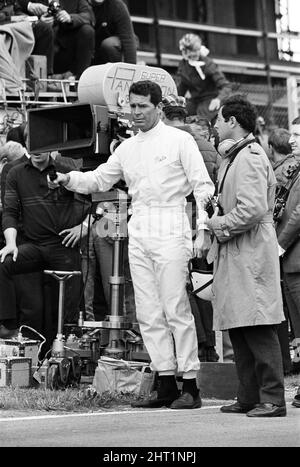 Dreharbeiten zum MGN-Film „Grand Prix“ bei Brands Hatch in Kent im Juli 1966. Schauspieler James Garner ist der amerikanische Grand-Prix-Fahrer Pete Aron, der von seinem Jordan-BRM-Rennteam gefeuert wird und für das japanische Yamura-Team fährt. Im Bild: Während der Dreharbeiten musste James Garner seinen Rennwagen (kein Stunt-Mann) für 1/2 eine Meile rund um Brands Hatch Circuit fahren, während er in Brand war. James hielt kurz nach der Ziellinie an und sprang aus dem Cockpit, als Flammen das Auto umschlingen. Feuerwehrmänner waren bereit, die Flammen zu löschen. James Garner ist während der Dreharbeiten zu diesem Film für £1million versichert. Stockfoto