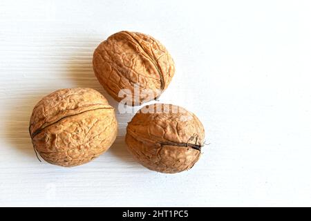 Walnüsse (Juglans regia) in Schale auf weißem Holzhintergrund, Nahaufnahme, Draufsicht. Stockfoto