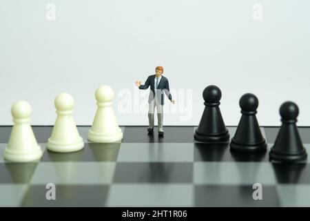 Miniatur Menschen Spielzeug Figur Fotografie. Strategieentscheidungskonzept. Ein scharfmütiger, unsicherer Geschäftsmann steht über dem Schachbrett mit schwarz weißem Schachbrett. Stockfoto