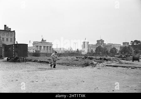 Szenen in Ost-Berlin, vier Jahre nach Beginn der Arbeiten am Bau der Berliner Mauer, die Ost und West trennt. Ein Mann, der durch eine heruntergekommene Gegend mit dem Brandenburger Tor und dem Reichstag im Hintergrund läuft. 26. Mai 1965. Stockfoto