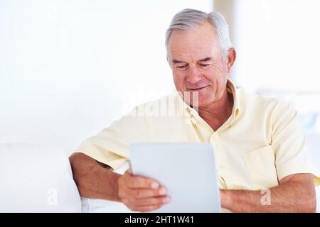 Reifer Mann mit Tablet-PC. Schöner reifer Mann mit Tablet-PC, während er auf der Couch sitzt. Stockfoto
