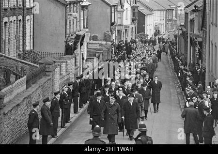 Aberfan - 27.. Oktober 1966. Trauernde gehen durch die Straßen, auf ihrem Weg zum Friedhof, um an der Massenbesetzung für die Opfer der Schlammrutsche-Katastrophe von Aberfan teilzunehmen. Als Zeichen des Respekts sind die Straßen mit Mitgliedern der Notdienste gesäumt. Die Katastrophe von Aberfan war ein katastrophaler Einsturz einer kollidierenden Beute im walisischen Dorf Aberfan, in der Nähe von Merthyr Tydfil. Er wurde durch eine Ansammlung von Wasser im angesammelten Fels und Schiefer verursacht, die plötzlich in Form von Schlamm bergab zu rutschen begann und am 21.. Oktober 1966 die Pantglas Junior School darunter verschlang und 116 Kinder tötete Stockfoto