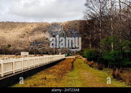 Ein Schmalspurzug nähert sich einer Kurve vor einem verlassenen Schiefersteinbruch, der das Gesicht eines Berges im Snowdonia National Park umschnappt Stockfoto