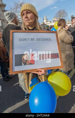 London, Großbritannien. Februar 2022. Eine Frau hält ein gerahmtes Schild mit der Aufschrift „LASS DICH NICHT TÄUSCHEN. [Putin] IST Ein KANNIBALE“ bei einer öffentlichen Demonstration in London. Sie trägt einen gelben Strickmütze und einen beigefarbenen Mantel und hält blaue und gelbe Ballons, die die ukrainische Flagge symbolisieren. Hunderte versammeln sich zu einem Protest, um Solidarität mit der Ukraine vor der Downing Street zu zeigen. Penelope Barritt/Alamy Live News Stockfoto