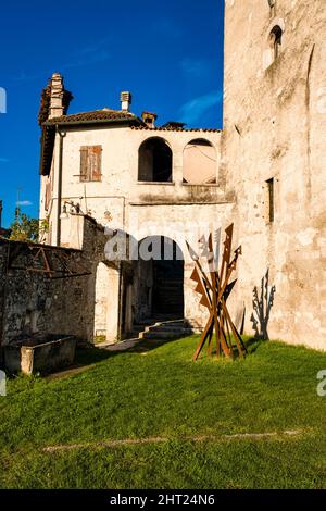 Metallkunstwerke im Innenhof des Schlosses Alboino mit Fassaden des Turms und einem angrenzenden mittelalterlichen Haus. Stockfoto