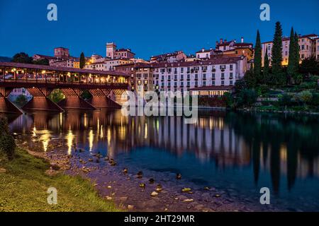 Die Brücke Ponte Vecchio, Ponte degli Alpini, die über den Fluss Brenta in Bassano del Grappa führt, mittelalterliche Häuser, die sich nachts im Wasser spiegeln. Stockfoto