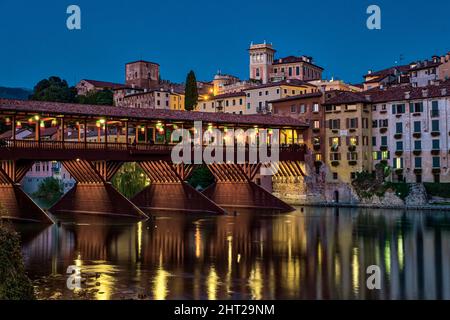 Die Brücke Ponte Vecchio, Ponte degli Alpini, die über den Fluss Brenta in Bassano del Grappa führt, mittelalterliche Häuser, die sich nachts im Wasser spiegeln. Stockfoto