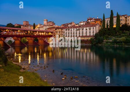 Die Brücke Ponte Vecchio, Ponte degli Alpini, die über den Fluss Brenta in Bassano del Grappa führt, mittelalterliche Häuser, die sich nachts im Wasser spiegeln. Stockfoto