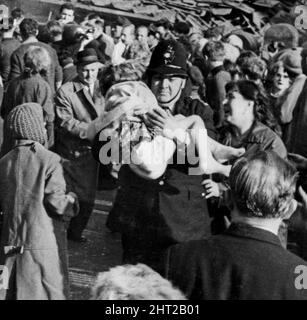 Aberfan - 21.. Oktober 1966. **BESCHNITTENE VERSION*** Polizist Victor Jones trägt ein kleines Mädchen (Susan Maybank) aus der zerstörten Schule, während die Frau ängstlich sieht, ob sie sie wiedererkennen kann - Aufnahme des Merthyr Express Fotografen Melville Parry Aufnahme vom 21.. Oktober 1966. Die Katastrophe von Aberfan war ein katastrophaler Einsturz einer kollidierenden Beute im walisischen Dorf Aberfan, in der Nähe von Merthyr Tydfil. Er wurde durch eine Ansammlung von Wasser im angesammelten Gestein und Schiefer verursacht, die plötzlich in Form von Schlamm bergab zu rutschen begannen und die Pantglas Junior School be verschlang Stockfoto