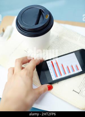 Arbeiten außerhalb des Büros. Smartphone mit Bar-Chart auf dem Bildschirm mit Einweg-Tasse, Stift, Zeitung und Clipboard. Stockfoto