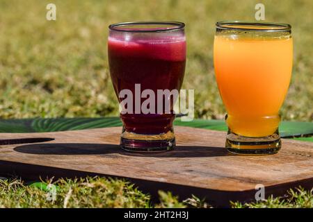 Granatapfelsaft und Orangensaft malta Saft in transparentem Glas auf Grasgrund. Anaar Juice santra ras auf Holzbrett Stockfoto