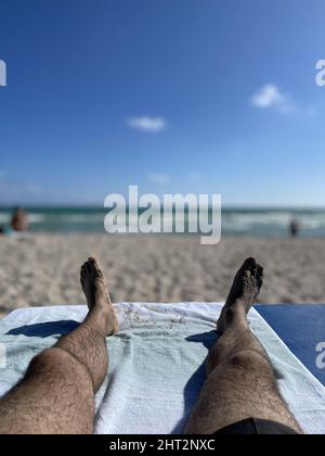 Vertikale Nahaufnahme der Füße des Mannes vor dem Hintergrund des Strandes. Stockfoto