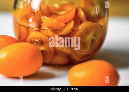 In Scheiben geschnittene Kumquat-Früchte in Sirup-Wasser im Glas, ganze Früchte auf dem Tisch, Nahaufnahme. Stockfoto