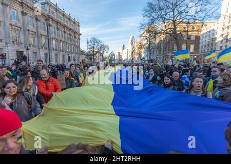 London, Großbritannien. 26. Februar 2022. Eine große Menschenmenge versammelt sich in Westminster, Großbritannien, zu einer öffentlichen Demonstration zur Unterstützung der Ukraine. Die Teilnehmer halten eine riesige ukrainische Flagge auf der anderen Straßenseite, von der viele blaue und gelbe Kleidung oder Gesichtsfarbe tragen. Die Kundgebung findet in der kälteren Jahreszeit in einem historischen städtischen Umfeld statt und symbolisiert Solidarität und bürgerliches Engagement. Demonstranten laufen mit einer riesigen ukrainischen Flagge entlang Whitehall. Penelope Barritt/Alamy Live News Stockfoto