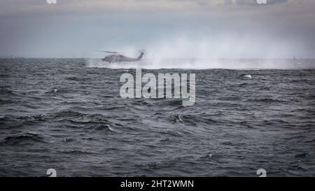 Ein Hubschrauber der US Navy MH-60, der niedrig und langsam fliegt, bevor er einen Rettungsschwimmer im Wasser absetzt, während er vor der Küste in der Nähe von Yokosuka, Japan, trainiert. Stockfoto