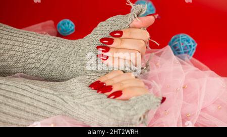 Crop Frau Hände mit roten polierten Nägeln. Nicht erkennbare Frau mit Maniküre in modischen Strickhandschuhen Stockfoto