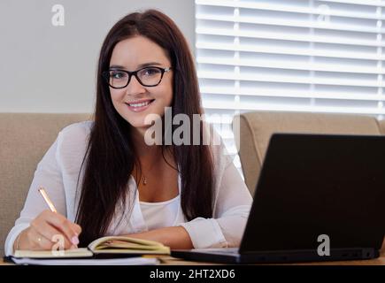 Das Aufschreiben der Dinge war so effektiv. Aufnahme einer jungen Frau, die Notizen schreibt, während sie von zu Hause aus arbeitet. Stockfoto