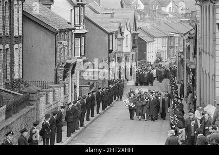 Aberfan - 27.. Oktober 1966. Trauernde gehen durch die Straßen, auf ihrem Weg zum Friedhof, um an der Massenbesetzung für die Opfer der Schlammrutsche-Katastrophe von Aberfan teilzunehmen. Als Zeichen des Respekts sind die Straßen mit Mitgliedern der Notdienste gesäumt. Die Katastrophe von Aberfan war ein katastrophaler Einsturz einer kollidierenden Beute im walisischen Dorf Aberfan, in der Nähe von Merthyr Tydfil. Er wurde durch eine Ansammlung von Wasser im angesammelten Fels und Schiefer verursacht, die plötzlich in Form von Schlamm bergab zu rutschen begann und am 21.. Oktober 1966 die Pantglas Junior School darunter verschlang und 116 Kinder tötete Stockfoto